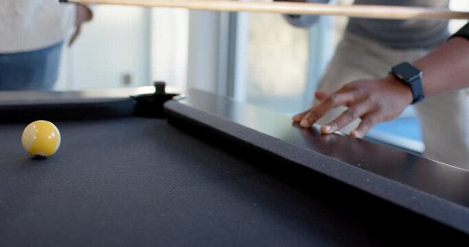 Diverse male friends playing pool, drawing cue and striking cue ball, then laughing by windows