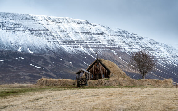 Historic grafarkirkja turf church in vast field, traditional icelandic architecture under a cloudy sky. Iceland landscape. Snowcap mountain