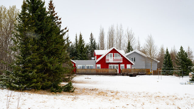 Red house and farmhouse with a balcony surrounded by snow and pine trees during winter. Iceland, Icelandic landscape winter