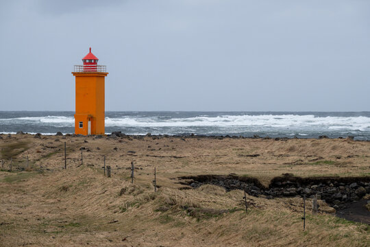 Stafnesviti orange lighthouse guiding ships along a stormy ocean coast under a grey sky. Reykjanes peninsula Iceland