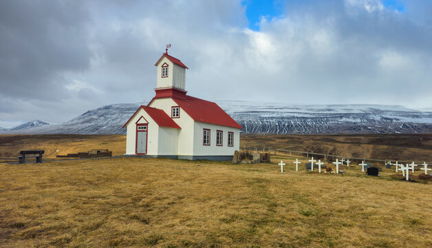 Rural church with red roof and white crosses in a graveyard, snowy mountains. Vididalstungukirkja church Iceland landscape Place of worship
