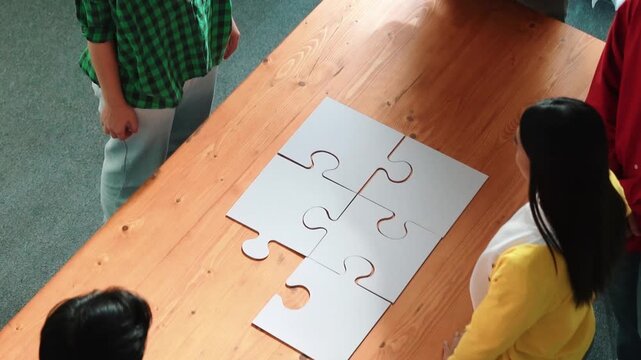 Top view of skilled business people gathering jigsaw piece together.Startup team with casual cloth standing at table while put jigsaw on table. Show unity, cooperation and team working. Convocation.