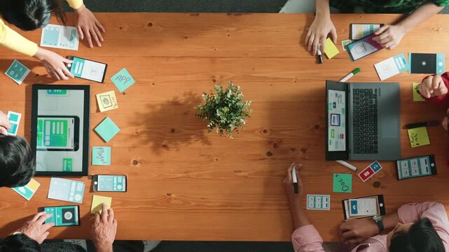 Programmer team brainstorm and plan Ux Ui design for mobile phone while present idea by using laptop at meeting. Software developer look at wireframe prototype while write at sticky note.Convocation.