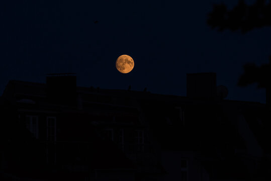 Glowing full moon rising over dark city building silhouettes in the pitch black night sky