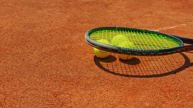 A yellow tennis ball and tennis racket lies on the clay court.