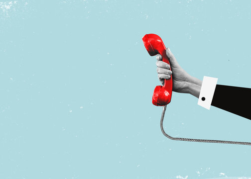 A hand holding a red landline, vintage telephone out of a laptop.