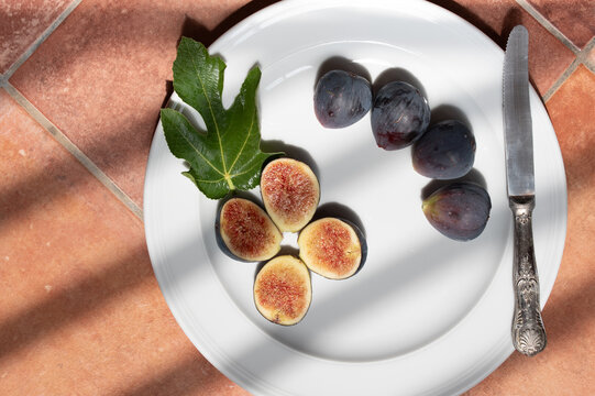 A shot from above of a plate in the kitchen. There are figs on the plate. The sun is shining on the plate, and shadows are visible.
