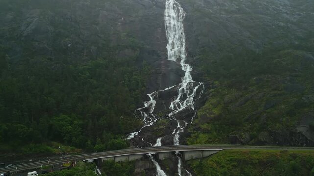 Majestic waterfall cascading down rocky cliffside in Norway, surrounded by lush greenery and rugged terrain, showcasing the natural beauty of the landscape