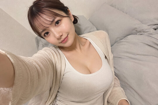 クリーム色のトップスでベッドから自撮りする女性