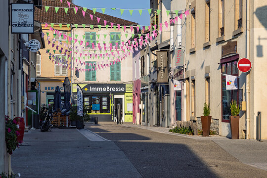 Montrevel-en-Bresse, France, July 30, 2026 - Charming empty village street adorned with pink and green bunting flags hanging above shops and businesses.