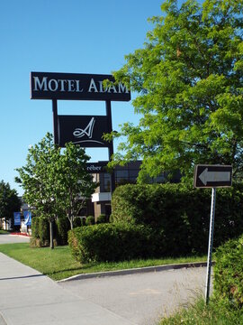 Gatineau, Quebec, Canada &ndash; June 21, 2026: A tall sign for "Motel Adam" stands near green trees, lush bushes, and a directional arrow sign under a blue sky on Bd Greber.