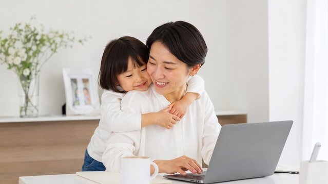 自宅でノートパソコンを使ってテレワークをする母親に、後ろから抱きつく笑顔の女の子。ワーママとワークライフバランスのコンセプト