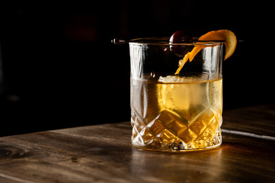 Close up of a classic old fashioned cocktail on a wooden background garnished with an orange twist and a cherry.