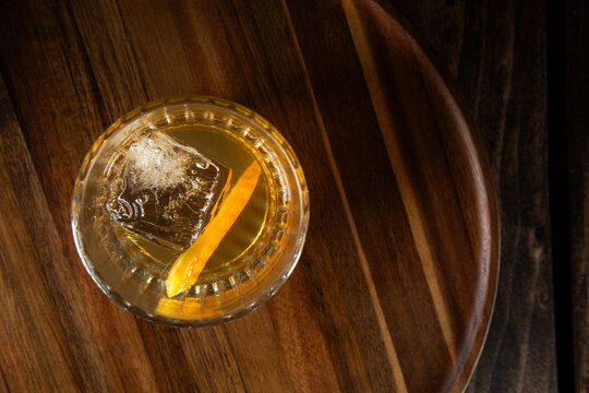Close up of a classic old fashioned cocktail on a dark wooden background garnished with an orange twist.