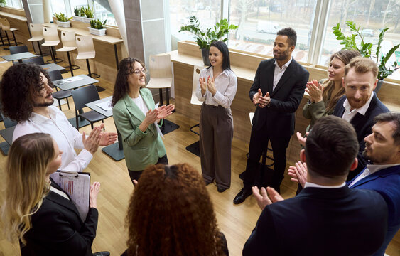 Business team meeting people applause success celebration. Smiling coworkers stand in a circle, clapping during corporate training in a modern office. Strong teamwork and motivation concept.