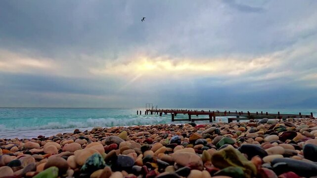 A soothing view of a pebble beach with clear blue waves under a cloudy sky.