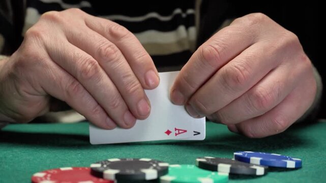 The hands show three playing cards with ace symbols, while multi-colored poker chips are scattered across a green felt table, illustrating the ongoing action of a card game