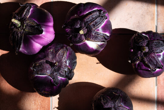 Several eggplants are lying side by side in the kitchen. The purple fruits are round and spherical.