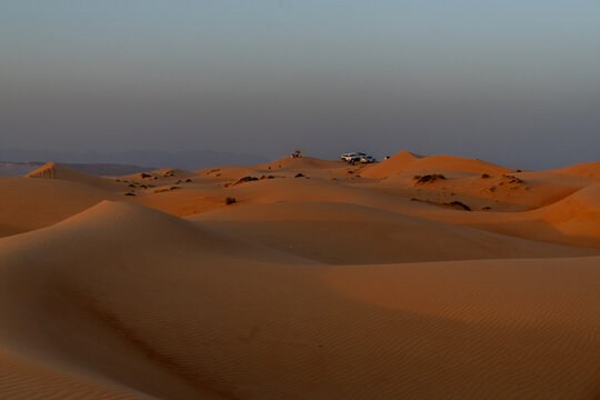 View of the golden sand dunes of Bidiyah with parked vehicles under a clear sky in Bidiyah, Ash Sharqiyah North G, Oman.