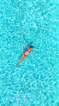 Top down view of a woman in pink swimsuit laying on her back in the pool.