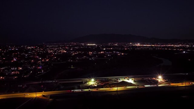Aerial footage of active construction along 2100 North in Lehi, Utah. Bright floodlights illuminate machinery, new roadway, equipment, and city lights.