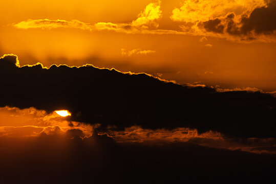 View of a vibrant sunset with glowing orange light filtering through dark clouds in Jahanian, Pakistan.