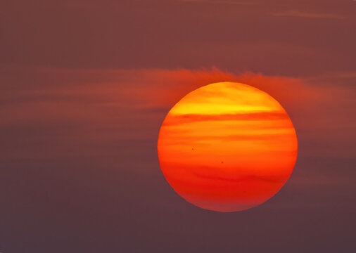 View of a vibrant orange sun setting behind thin clouds in the sky over Jahanian, Pakistan.