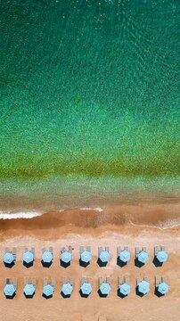 Top-down view of sandy beach with sun umbrellas and turquoise sea water