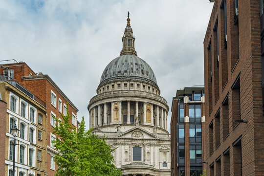 View of St. Paul's Cathedral with its iconic dome framed by modern and historic brick buildings under a cloudy sky in London, England, United Kingdom.