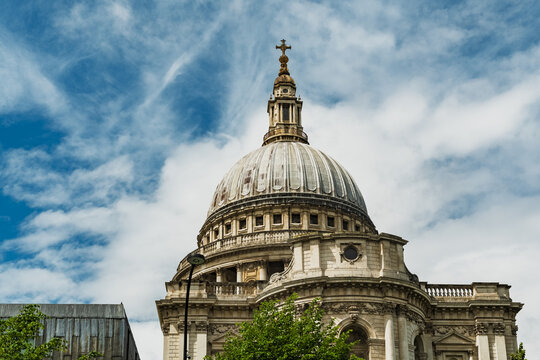 View of the iconic dome of St. Paul's Cathedral with its stone architecture and cross, set against a bright blue sky with clouds in London, England, United Kingdom.