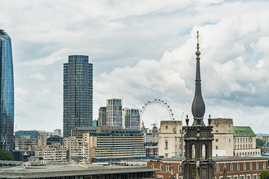 View of the London skyline featuring modern skyscrapers, the London Eye observation wheel, and a historic church spire under a cloudy sky in London, England, United Kingdom.