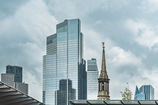 View of the Leadenhall Building and the historic spire of St. Helen's Bishopsgate set against a cloudy sky in London, England, United Kingdom.