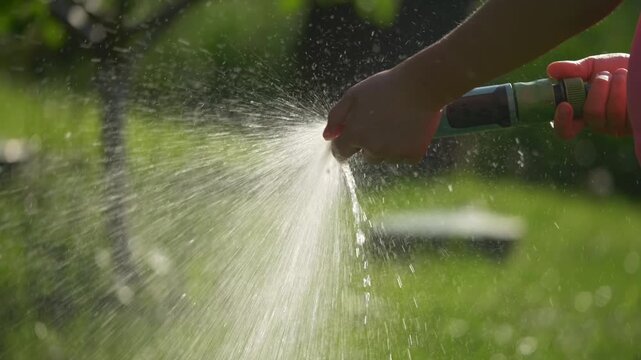 Close up of child blocking water hose with thumb making wide splash
