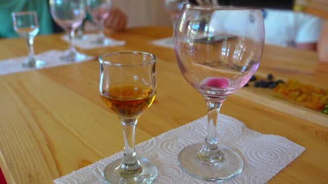 Close-up of a person pouring a golden amber liqueur from a bottle with a pour spout into a small tasting glass, part of a professional spirits tasting event on a wooden table