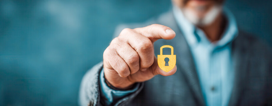 Man holding a yellow lock symbol while dressed in a suit and standing in front of a blue background in an office setting