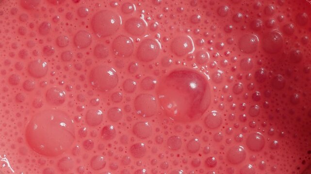 Red frothy bubbles on surface of blended berry smoothie, vibrant full-frame macro texture 