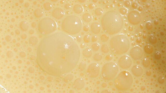 Frothy yellow bubbles covering surface of freshly blended smoothie, full-frame macro texture