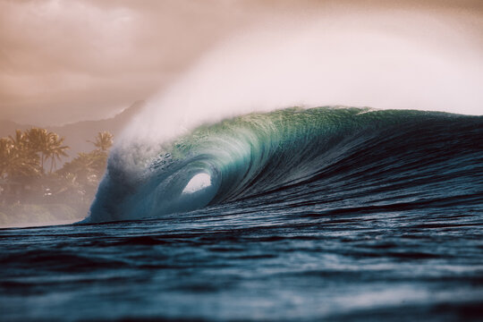 Large wave breaking over a reef at sunset with a beach in the background, Oahu, Hawaii, USA