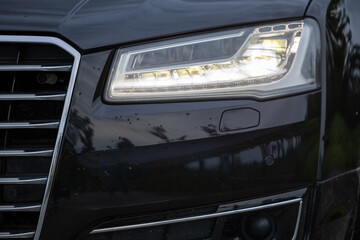 Close-Up Of Luxury Black Car Front Headlight And Chrome Grille With Illuminated LED Lighting © Boris