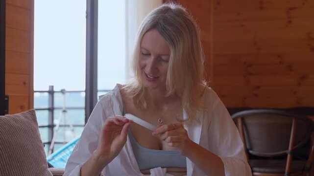 Smiling blonde woman sitting comfortably at home, neatly filing her nails with a nail file during personal beauty treatment, creating the perfect manicure and relaxing moment of self-care