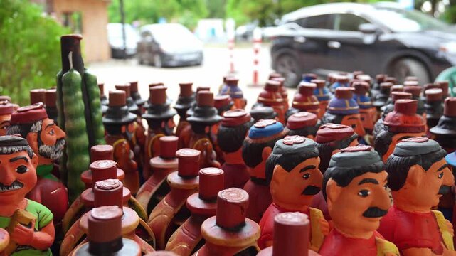 Colorful handmade georgian ceramic wine jugs and souvenirs, shaped like people in traditional clothing, displayed for sale at an outdoor market stall in a wooden crate for tourists to purchase