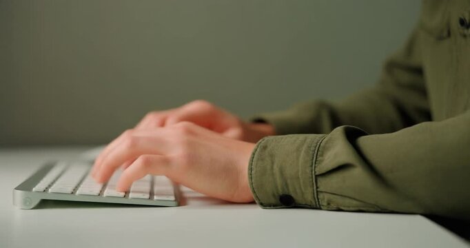 Person in olive green shirt typing on white computer keyboard