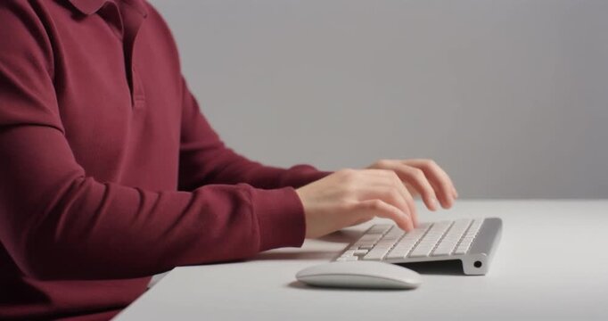 Person wearing red polo shirt typing on white computer keyboard