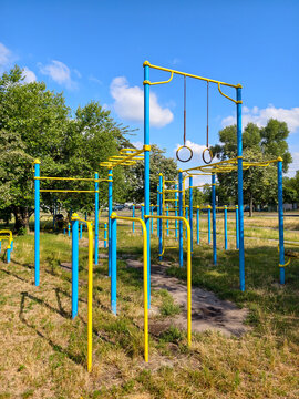 Yellow and blue outdoor exercise complex with stationary equipment gymnastic rings pull up bars and parallel bars in a residential neighborhood for strength training and recreation