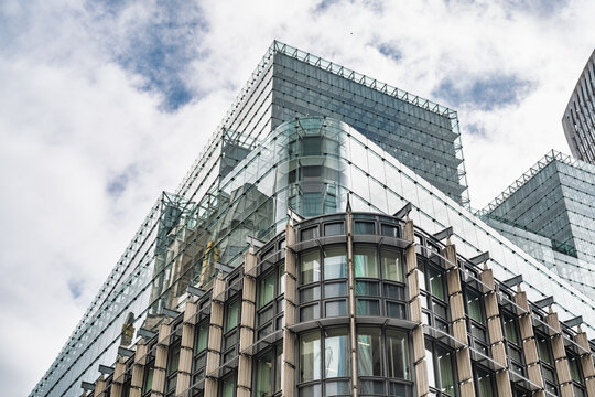 View of the modern glass architecture of a commercial building with stone structural details under a cloudy blue sky in London, England, United Kingdom.