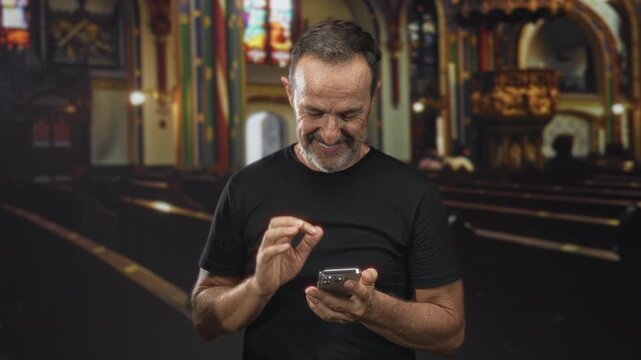 Middle aged hispanic man tapping smartphone with fingers while smiling and scrolling in ornate church building pews, looking down at screen; serenity reflection connection.