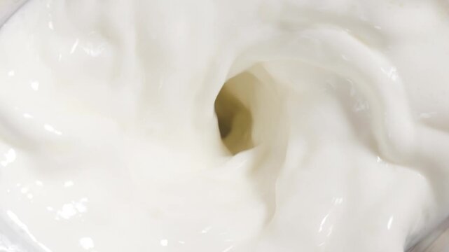 Creamy white milk swirling into a vortex inside blender jar, overhead macro of liquid motion