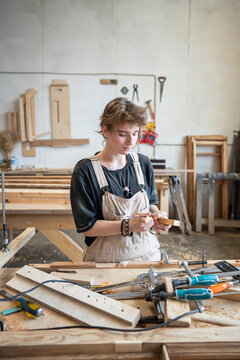 Process of restoration in woodworking studio, woman carpenter measures blocks for patch with ruler, skilled female restorer at worktable precisely preparing wooden details during restoration stage.