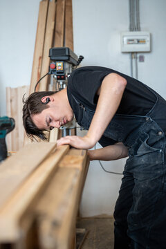 Skillful craftsman restorer engaged in process or repairing old wooden window frame in restoration workshop, worker attentively checking and comparing fitting of wooden boards replacement at workbench
