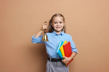 Pretty little girl with school bell and books on color background © New Africa